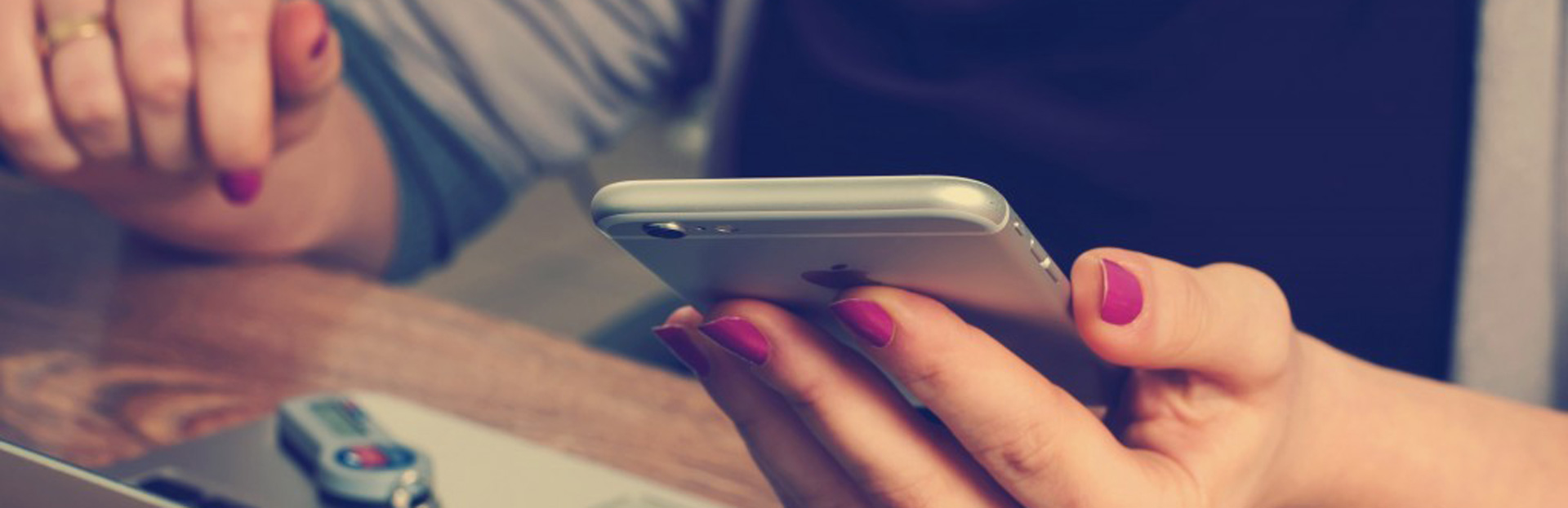 Manos de mujer sosteniendo un smartphone frente a un laptop